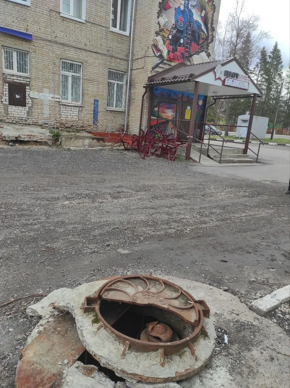 На фото — вход в детскую библиотеку в Шумерле напротив администрации округа. За фасадной «красотой» скрывается обрушившийся парапет, открытые люки и плохие дорожные заплатки; местные связывают это с неэффективностью местных властей и низкими рейтингами руководства региона.